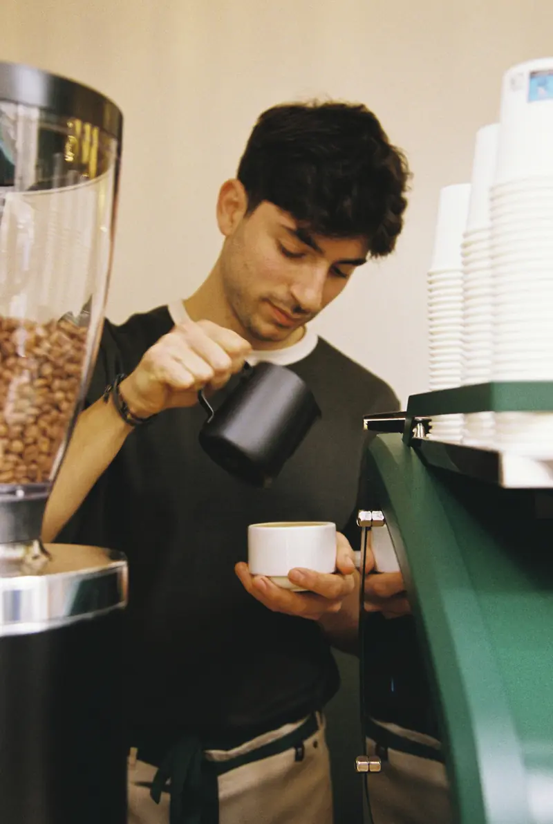Barista sosteniendo una taza junto al molino de café y la máquina verde
