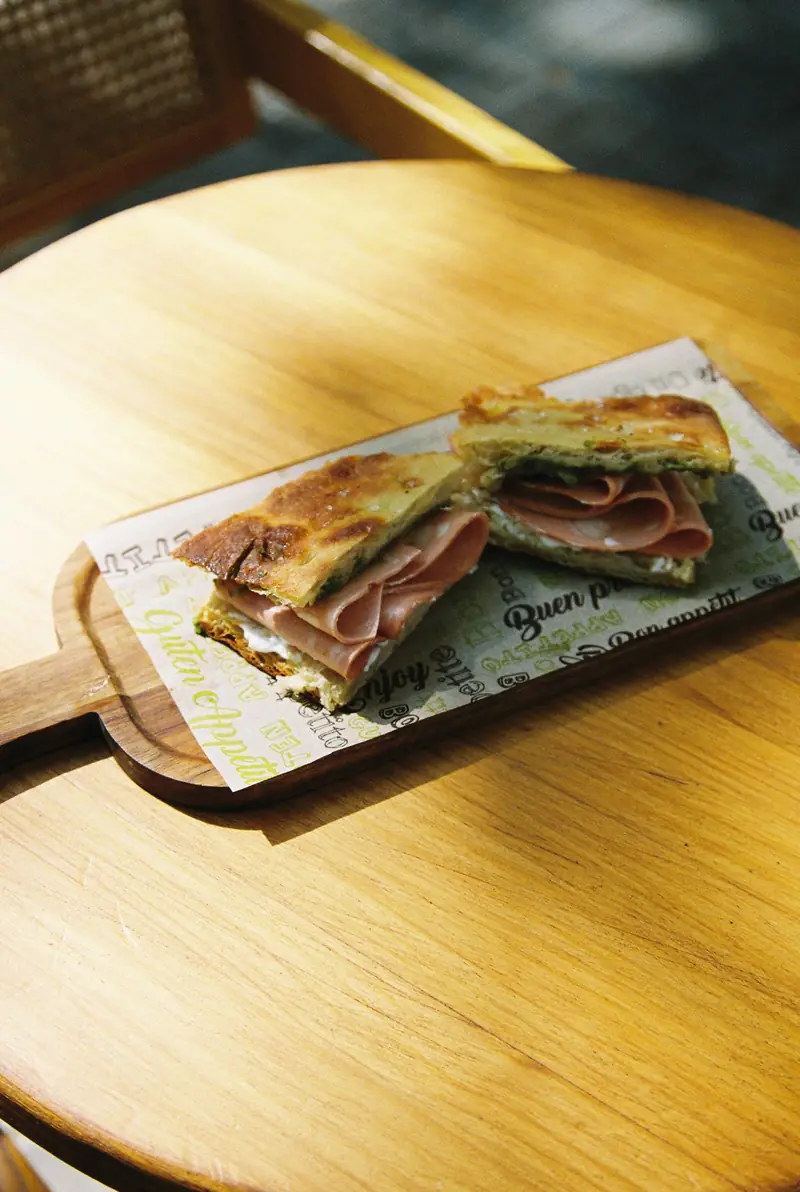 Focaccia de mortadela partida por la mitad sobre una tabla, al sol, en una mesa de madera