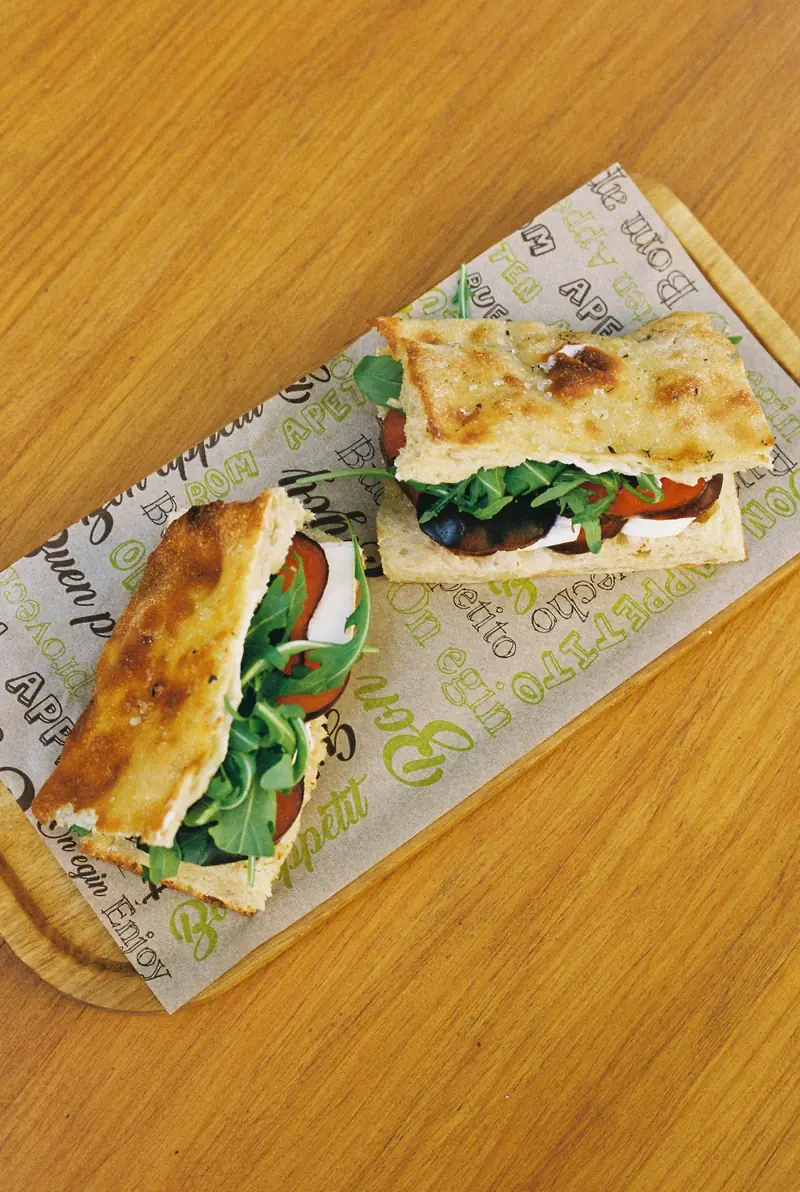Dos medias focaccias rellenas con rúcula y tomate sobre papel de envolver