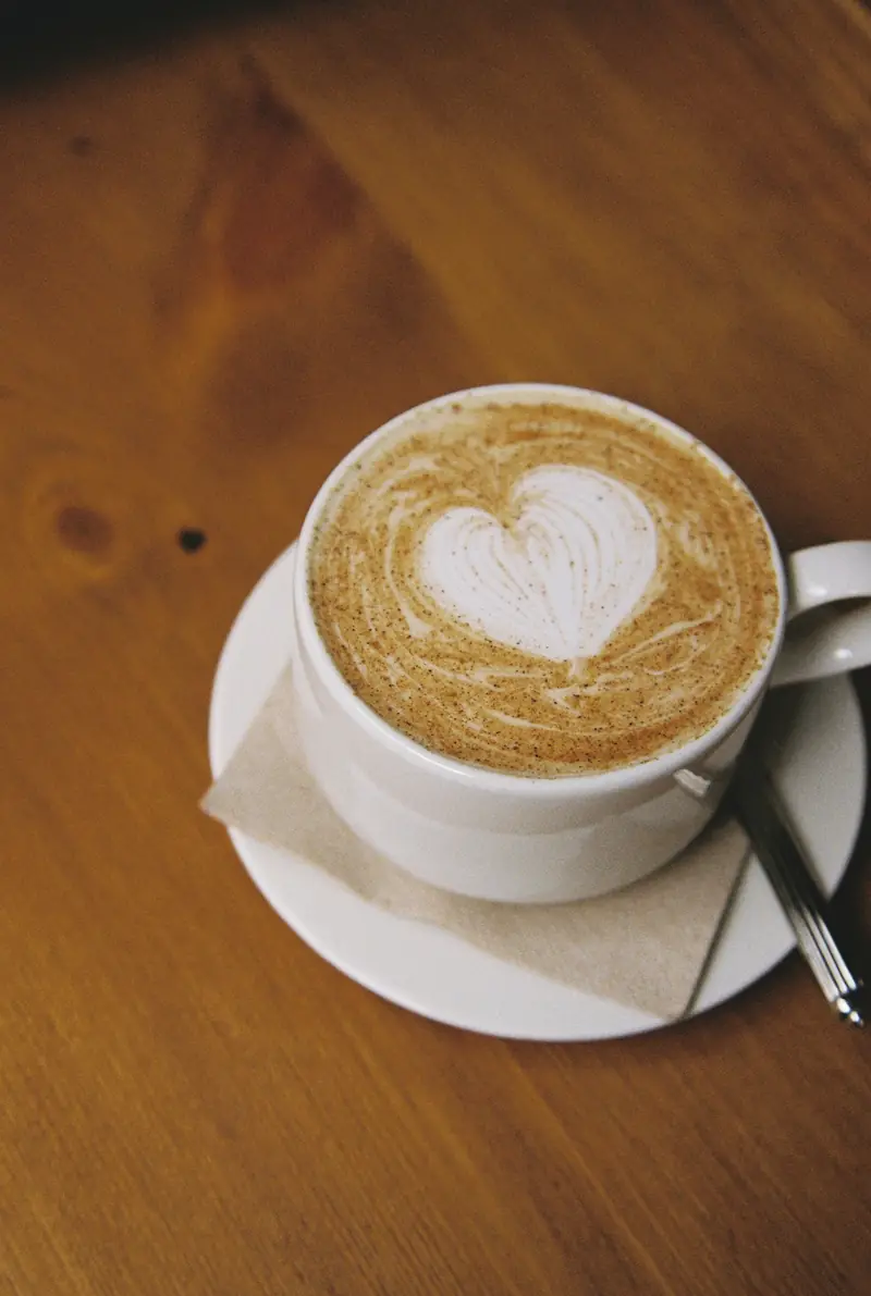 Café con leche con arte latte en forma de corazón, visto desde arriba, sobre una mesa de madera