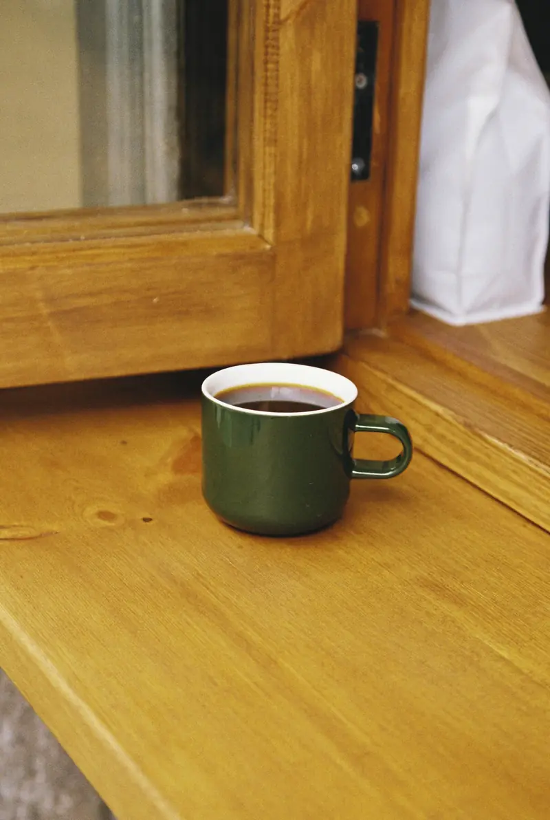 Taza verde de café sobre la barra de madera junto a la ventana