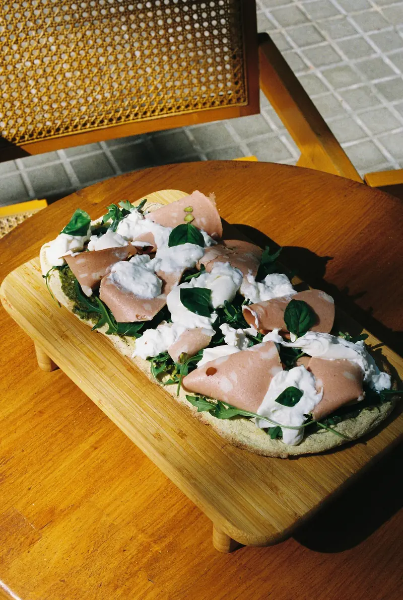 Pizza de mortadela con stracciatella y albahaca sobre una tabla de madera, en una mesa con mantel de cuadros