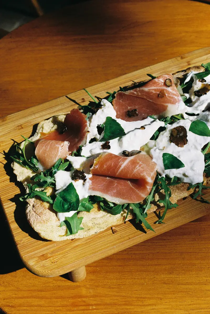 Pizza con prosciutto, stracciatella, rúcula y trufa sobre una tabla de madera