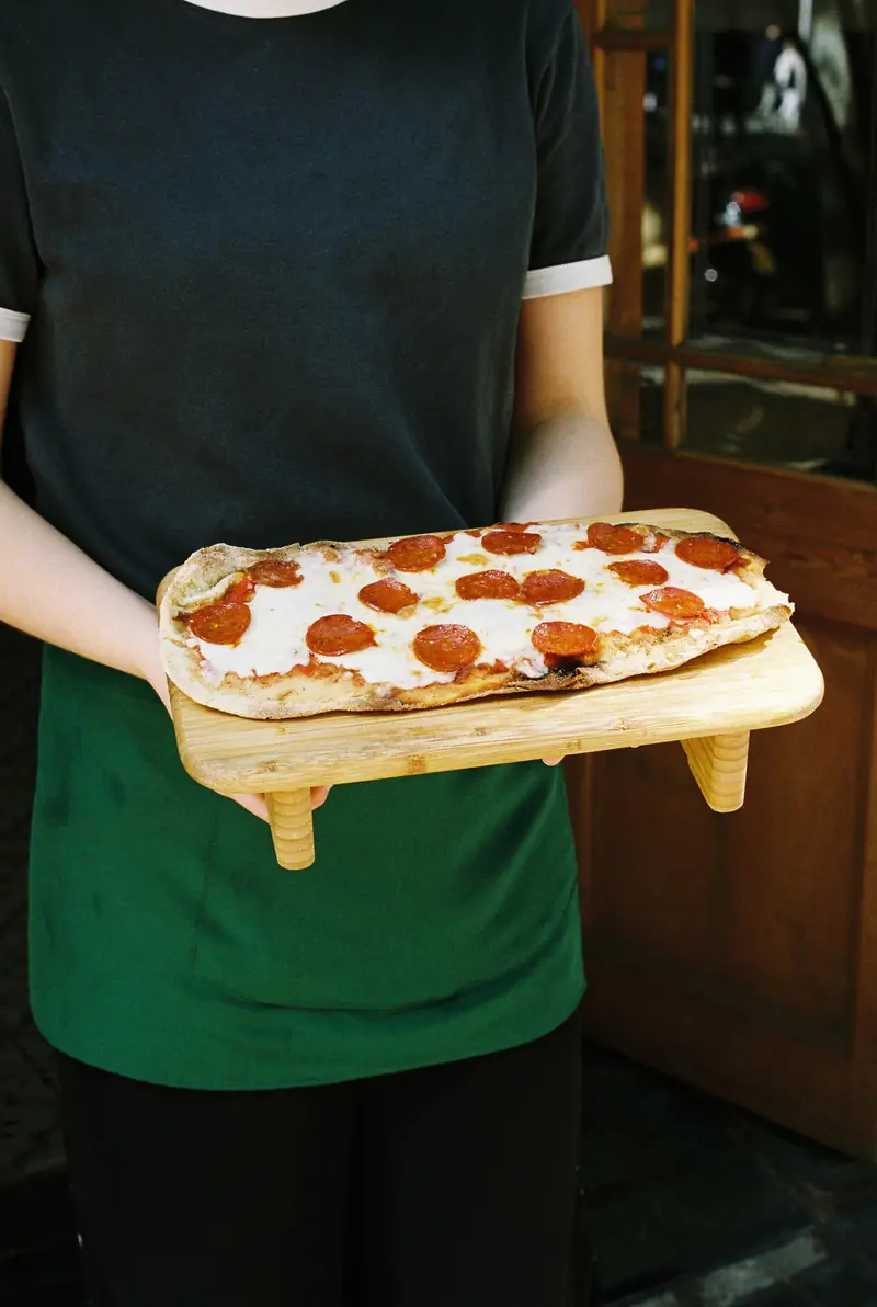 Una persona del equipo sostiene una pizza diavola sobre una tabla de madera
